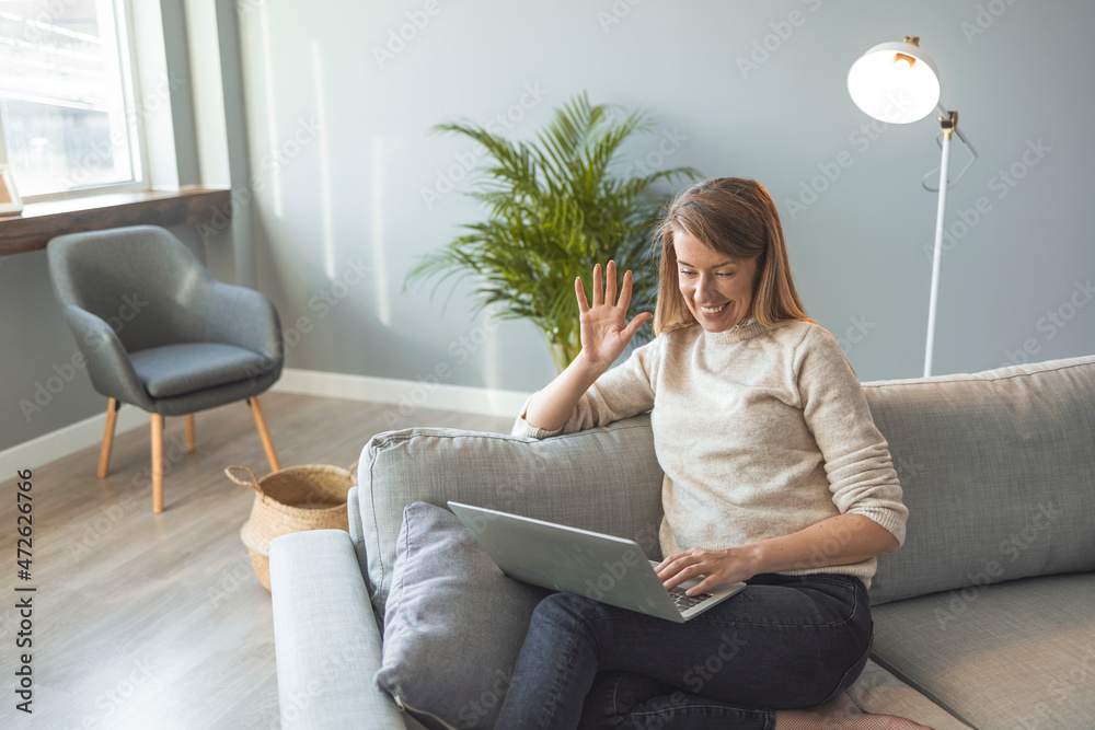 Woman waving while looking at camera at home. Woman waving on video call. Woman holding video call, gesturing hi to friends, relatives or parents.  Smiling girl having online interview with employer.