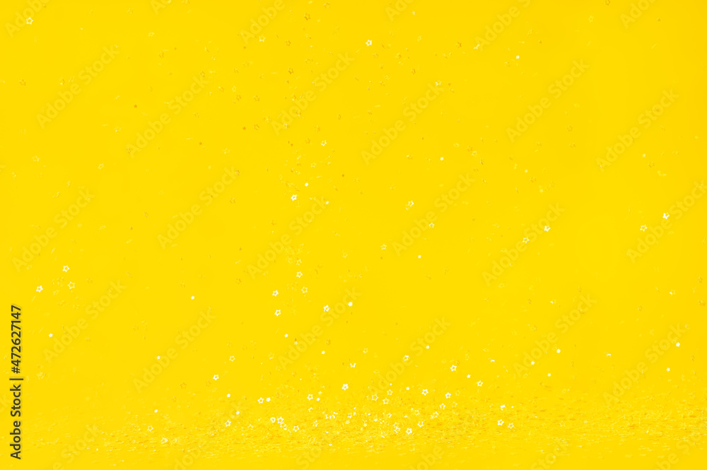 Falling shiny golden star shaped confetti on yellow background. Great backdrop for any holiday or event with copy space.