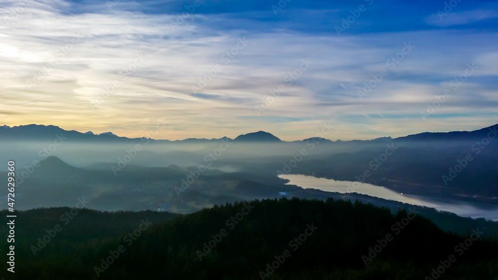 A view on the Woerthersee lake from the observation deck of Pyramidenkogel Tower. Lake is reflecting the last beams of sun for this day. Golden hour. The surrounding hills are shining gold. 
