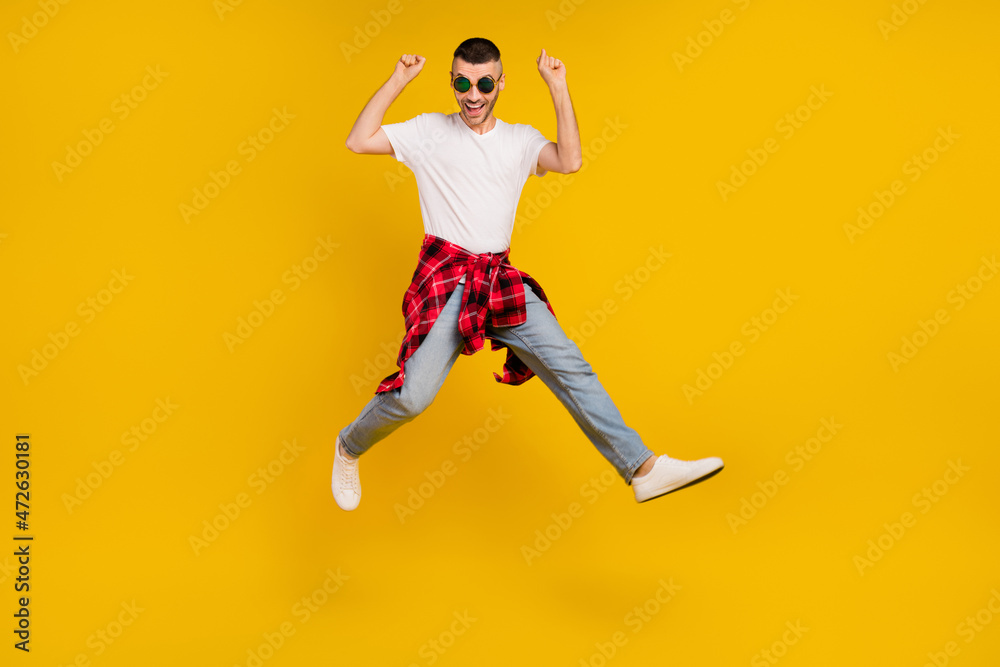 Full body photo of young funky man jump up winner enjoy wear plaid shirt tied on waist isolated on yellow color background