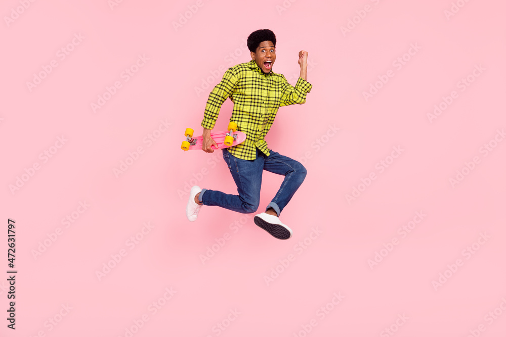 Full size photo of excited afro american man longboard jump wear casual clothes win isolated on pink color background