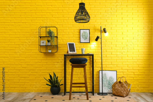 Obraz na plátně High wooden table with tablet and stool as stand up workplace near yellow brick wall