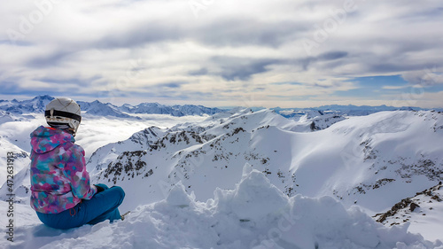 Snowboarding girl sitting on the snow in Moelltaler Gletscher, Austria, enjoying the view. Lots of snow in the mountains. Endless Alps chain. Winter wonderland, paradise. Calmness and happiness. photo