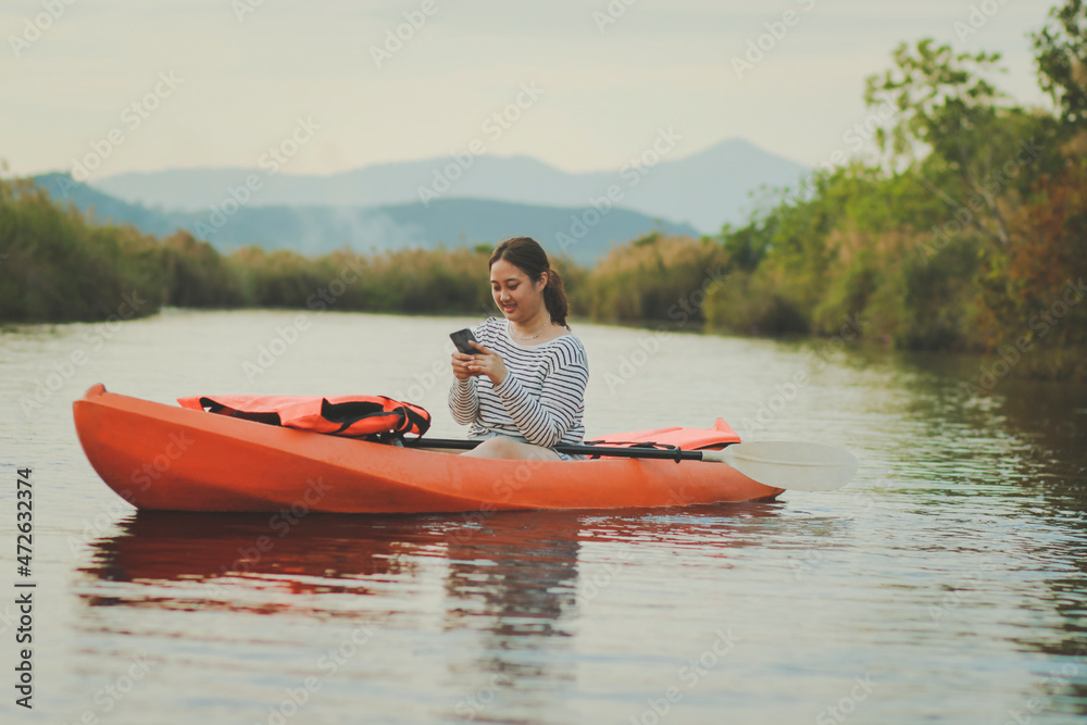 asian younger woman reading message while sailing kayak in river