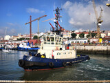 Harbour tug manoeuvring in harbour with cityscape background.