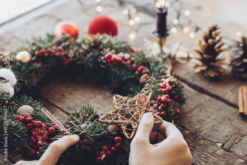 Woman making Christmas wreath, Fir handmade Chirstmas wreath with wooden star and red berries, rustic advent decoration, Christmas wreath making workshop photo