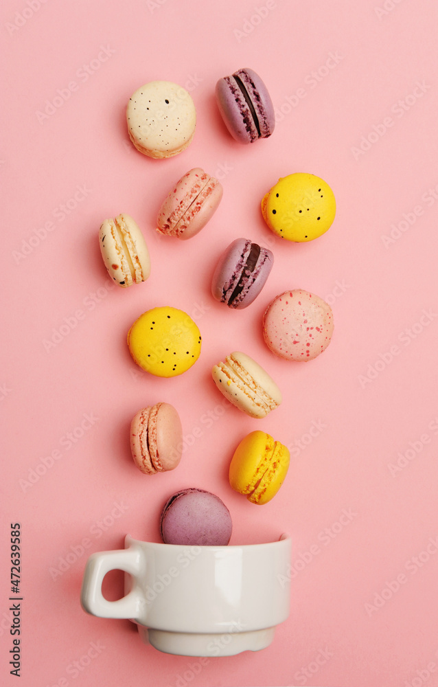 Colorful french macarons fall in white cup on pink background