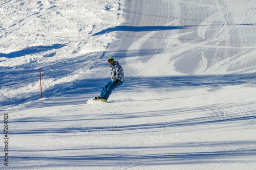 A man slides down the slope of a ski slope on a snowboard. There is no one else on the slope but him. Winter sports during the vacations.