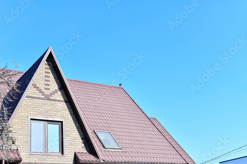 A house with a roof made of metal tiles against the background of an empty sky.