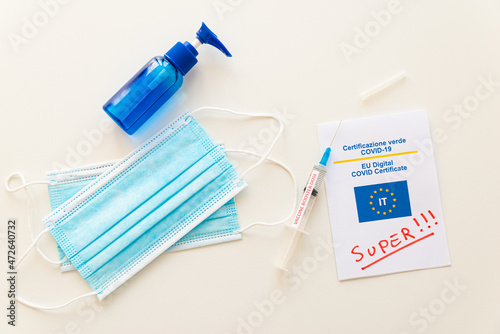 Covid Green Pass with text "super", blue mask, hand sanitizer, and syringe labeled "vaccine booster dose" on a white surface. Introduction of the super green pass and third dose of the vaccine, or boo