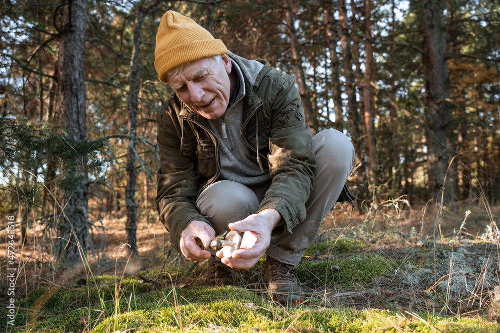 Old man sitting with mushroom on the ground in the forest Old man sitting with mushroom on the ground in the forest