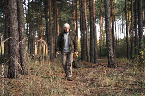 Elderly man walking at the forest with the background of trees and enjoying