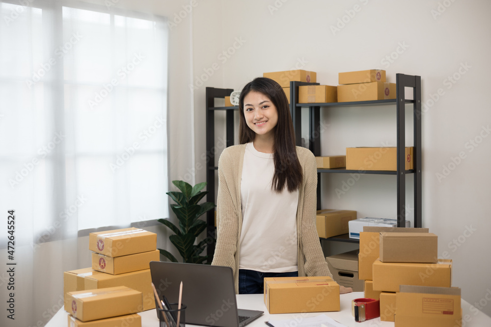 Beautiful young asian entrepreneur standing pose smiling to camera. Female small Business owner with box working at home. Startup freelance people with many parcel on background. Beautiful young asian entrepreneur standing pose smiling to camera. Female small Business owner with box working at home. Startup freelance people with many parcel on background.