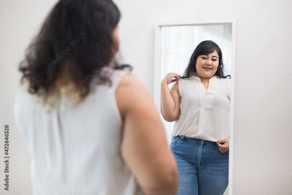 Body positive plus size female clothing. Body positive plus size woman happily and is proud of herself looking at mirror at home. Try wearing clothes that measure the size. Body positive plus size female clothing. Body positive plus size woman happily and is proud of herself looking at mirror at home. Try wearing clothes that measure the size.