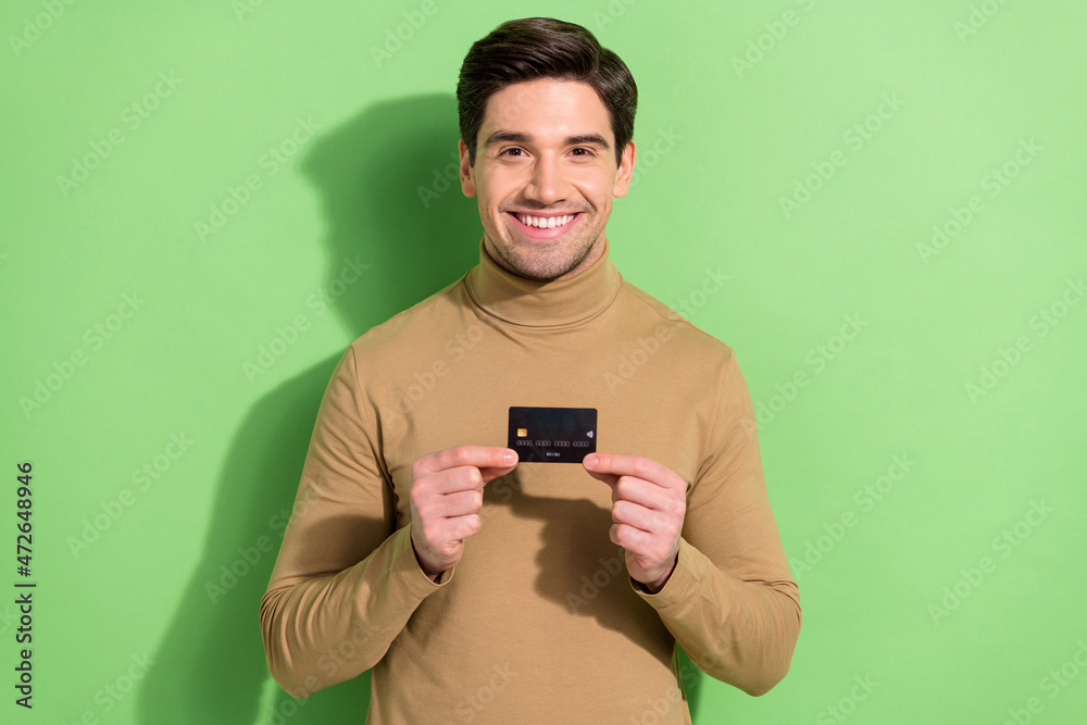 Photo of positive person hold demonstrate debit plastic card beaming smile isolated on green color background Photo of positive person hold demonstrate debit plastic card beaming smile isolated on green color background