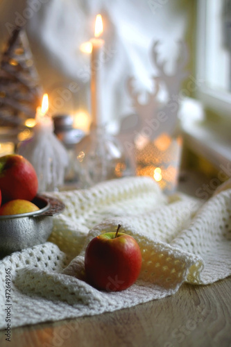 Bowl of apples and soft blanket with lit candles and Christmas decorations in the background. Selective focus.