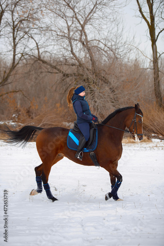 Equestrian country girl riding her bay horse in winter.