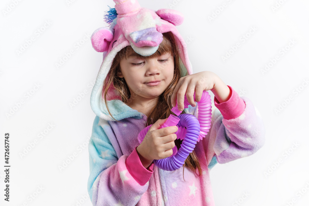 Cheerful little girl in unicorn pajamas plays in a popular toy poptube. An exciting children's game with multi-colored plastic pipes.