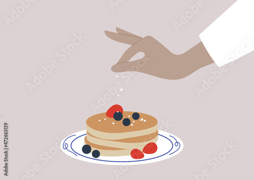 Hand sprinkling sugar powder on a stack of pancakes served with fresh berries, sweet breakfast food