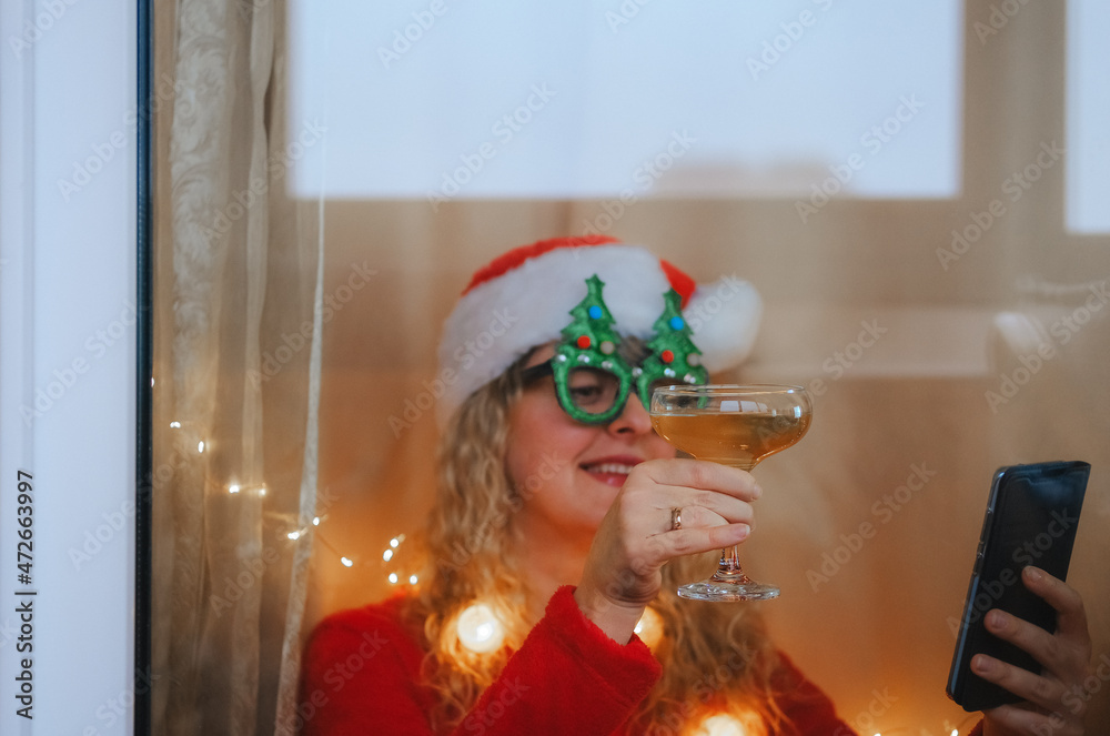 Woman in Santa hat and champane celebrating New Year's Eve at home making video call
