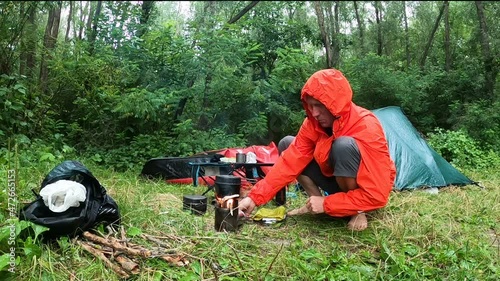 Man tourist prepares dinner on a wood stove in the rain time