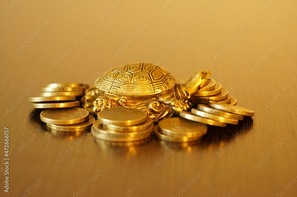 Metal turtle with coins on a gold background. A financial symbol of