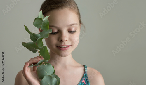 Beautiful cheerful smiling girl with eucalyptus leaf branch. Child with herbal plants. Kid with clean perfect skin, SPA, skincare and wellness concept. selective focus