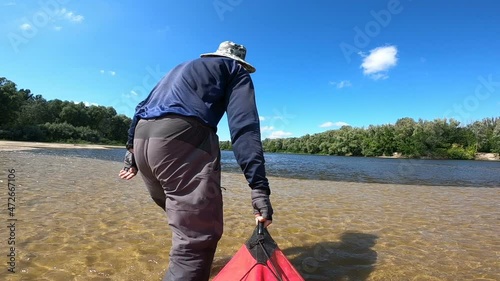  Man tourist tows a kayak  aground on river bank.