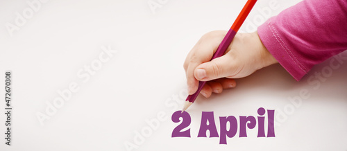 A child's hand writes 2 april in a lilac pencil. Banner with copy space photo