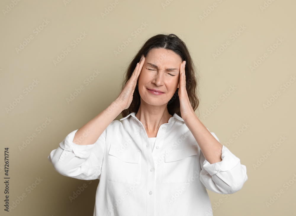 Mature woman suffering from headache on beige background