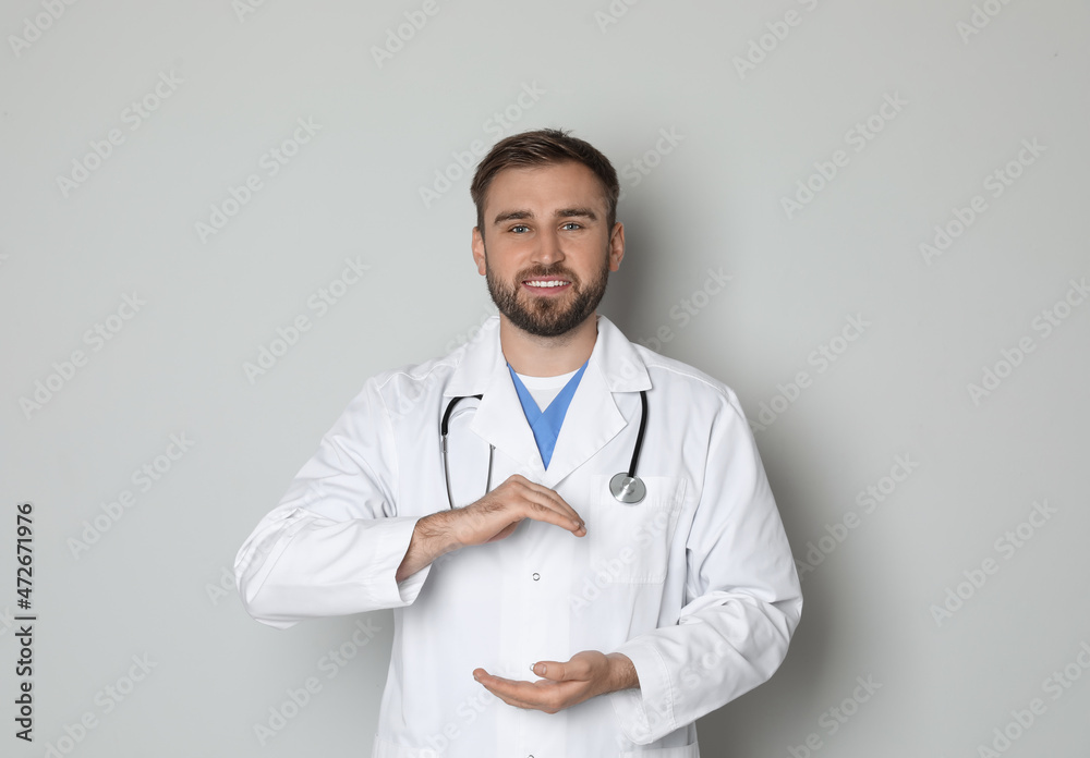 Young doctor holding something on light grey background Young doctor holding something on light grey background