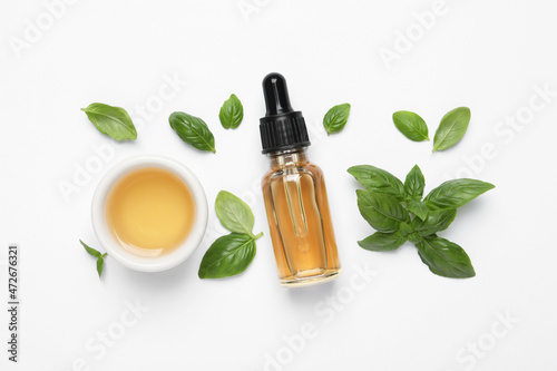 Essential basil oil with fresh leaves on white background  flat lay