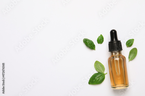 Bottle of essential basil oil and fresh leaves on white background  flat lay. Space for text