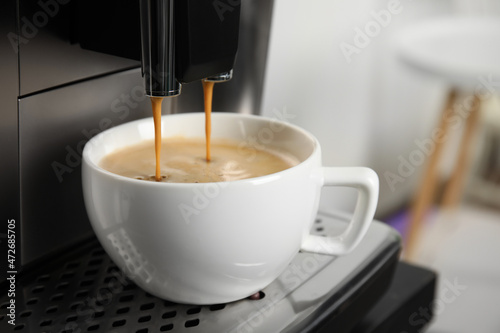 Espresso machine pouring coffee into cup against blurred background, closeup