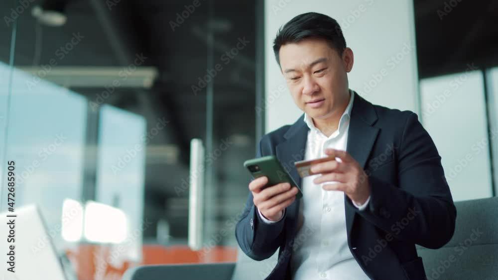 Happy asian business man shopping online customer paying by bank credit card sitting in a modern office Purchase service, booking. Satisfied Cheerful Male employee worker Using mobile phone smartphone