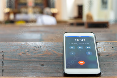 Calling God with a mobile phone on the table of a prayer bench in the church with altar.