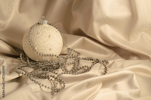 Christmas and New Year concept. Christmas card with ball on ivory silk background. Christmas bauble and copy space for text