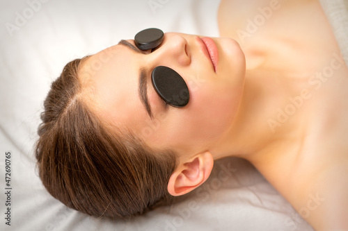 Black massage stones lying on the eyes of the young caucasian woman. Facial massage in a spa