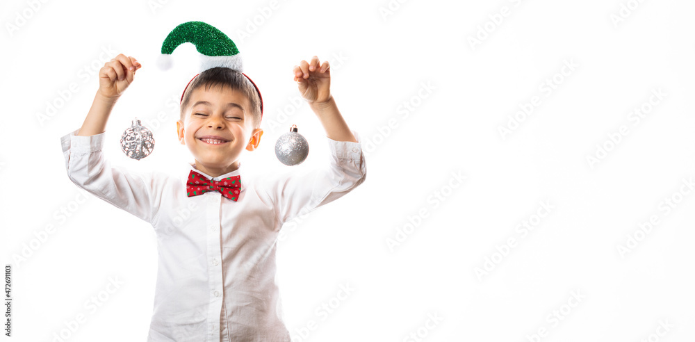 Little funny boy in Santa Claus headband holding Christmas decoration balls in hands and smiling against white background Little funny boy in Santa Claus headband holding Christmas decoration balls in hands and smiling against white background