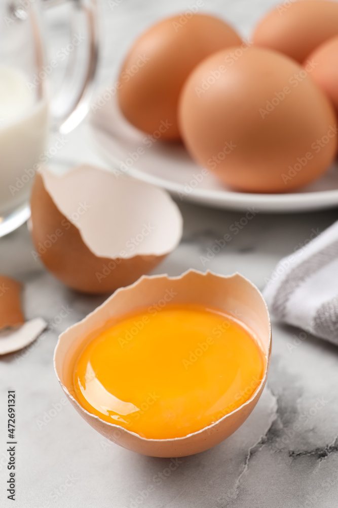 Cracked eggshell with raw yolk on white marble table, closeup. Space for text Cracked eggshell with raw yolk on white marble table, closeup. Space for text