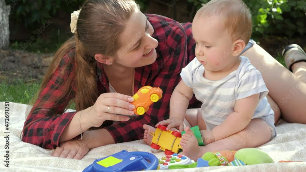 Happy smiling mother with little baby son playing toys on grass at park. Concept of child development, family having time together and parenting. Happy smiling mother with little baby son playing toys on grass at park. Concept of child development, family having time together and parenting.