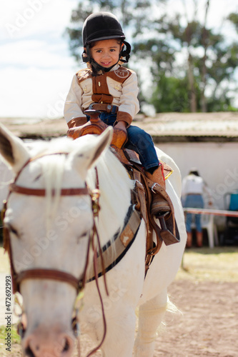 Cowboygirl wearing helmet riding a white horse in a riding school