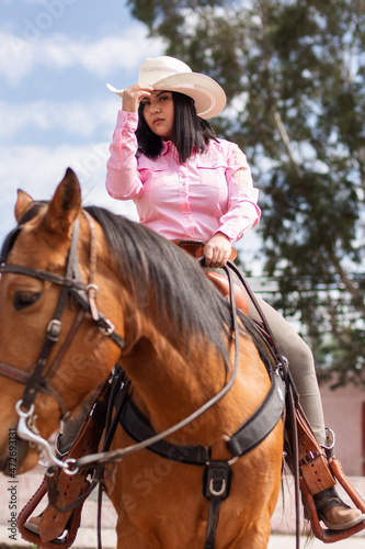 Cowgirl wearing boots and hat riding a horse outdoors