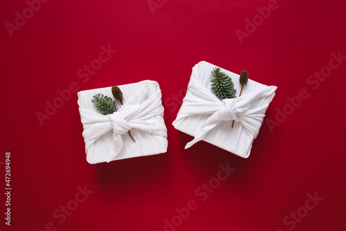 Eco and sustainable gift wrapping ideas. White gift boxes in cloth on red background. Christmas New Year backdrop with Furoshiki wrap and bokeh lights. Recycling concept and eco-friendly alternatives.