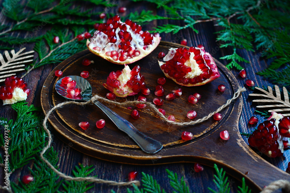 Bright red pomegranate grains on a wooden board against a background of fir branches