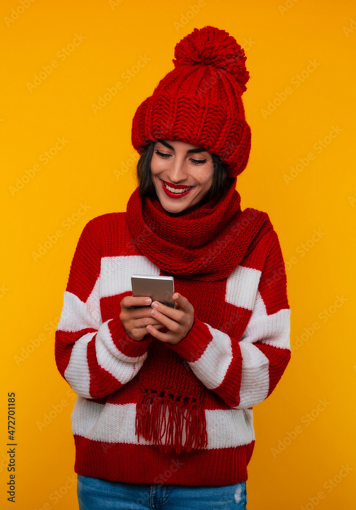 Close up portrait of happy smiling young modern beautiful woman in red winter hat and scarf while she uses her smart phone for chatting Close up portrait of happy smiling young modern beautiful woman in red winter hat and scarf while she uses her smart phone for chatting
