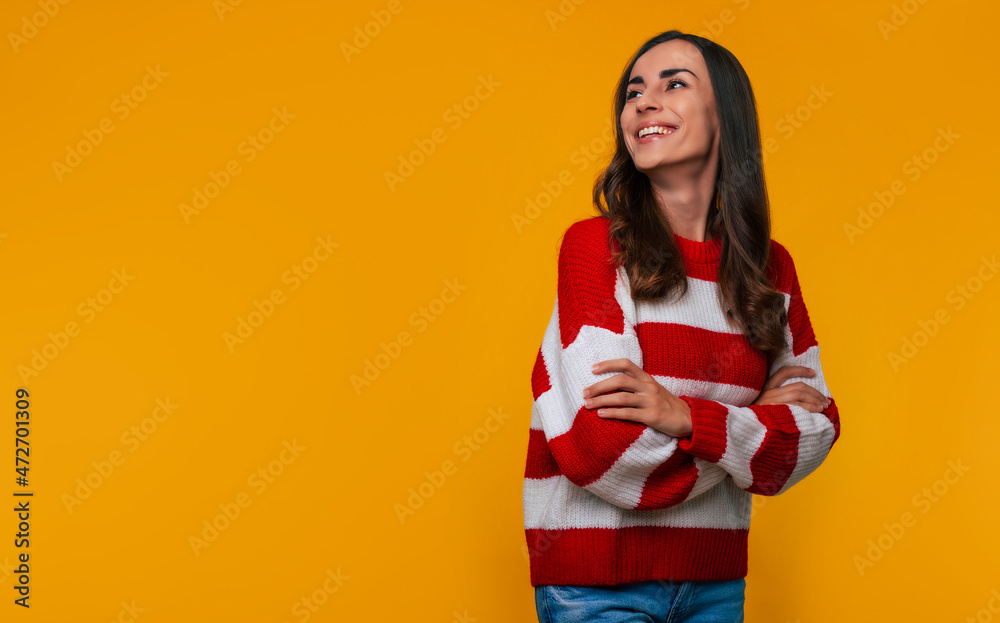 Close up photo of a beautiful smiling young woman in a sweater with crossed hands while she posing isolated on yellow background Close up photo of a beautiful smiling young woman in a sweater with crossed hands while she posing isolated on yellow background