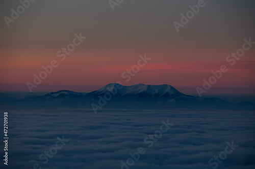 aerial view of evening sky with clouds and mountain tops covered with white snow.