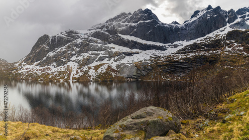 Europe, Norway. Snow covered mountains descend into a lake on Vestvagoy, a part of the Lofoten Islands in Nordland.