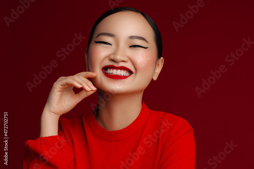 Overjoyed young korean model with red lips make up posing against red background.